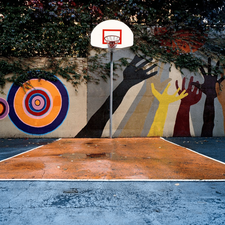 An outdoor basketball hoop set against a wall of colorful murals.